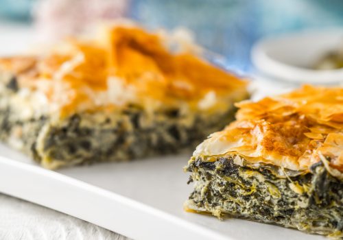 Greek pie spanakopita on the white plate on the white wooden table with  blurred accessorizes horizontal