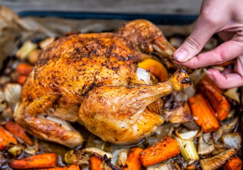 Roasted tied baked cooked whole chicken with woman removing string with fennel carrots vegetables and black pepper seasoning on skin